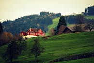 在薄雾缭绕的绿色乡村中，一座红色农舍坐落在连绵起伏的山丘和遥远的森林之间