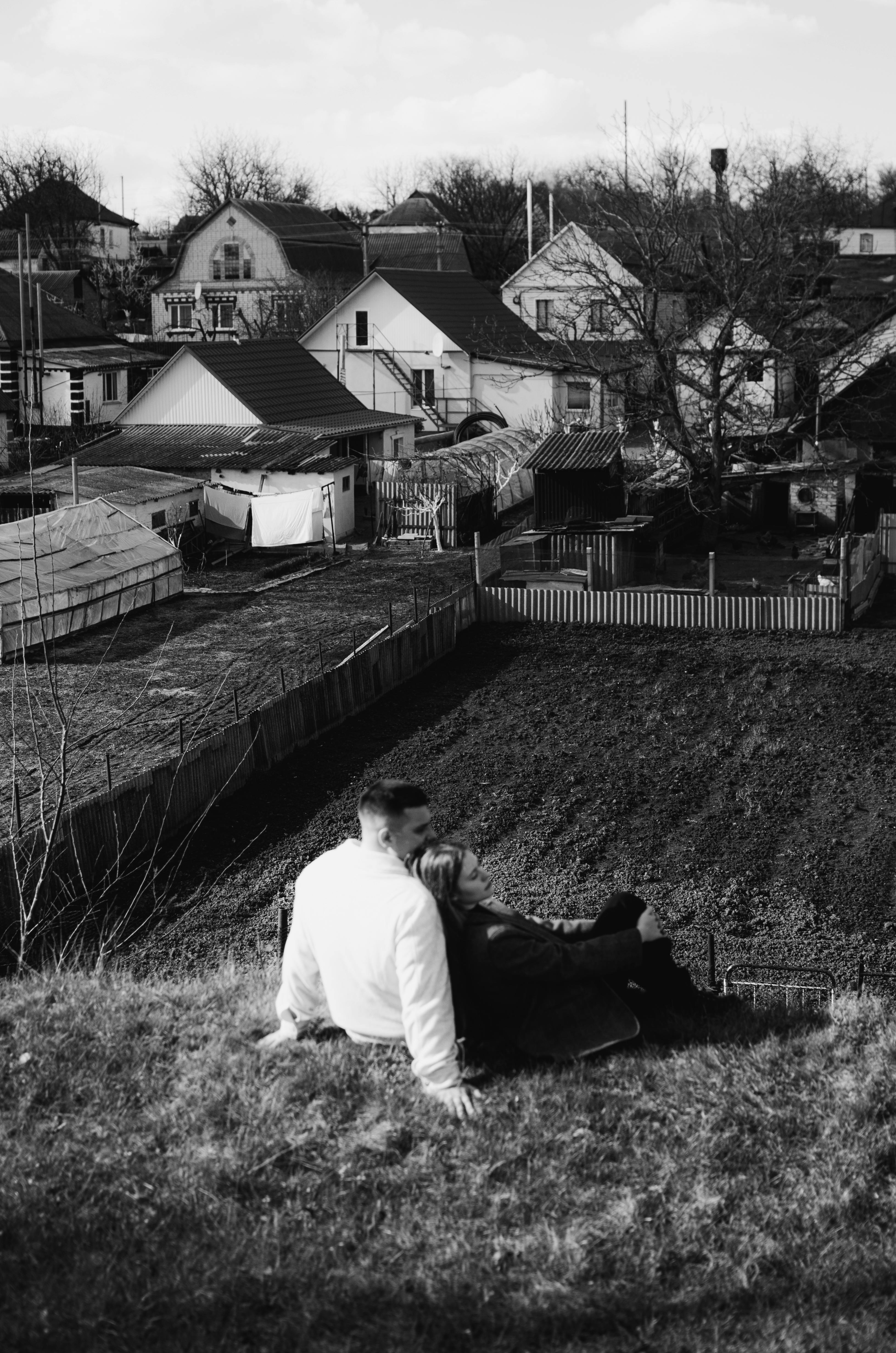 A couple peacefully sitting on a hill overlooking a rustic Ukrainian village.