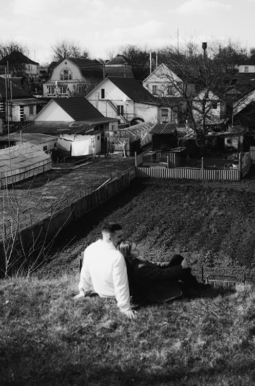 Couple Sitting on Hill over Field in Village