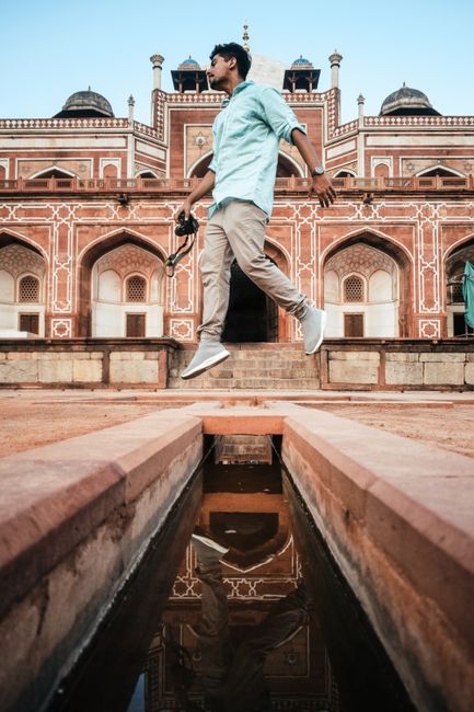 A man jumping with a camera in front of a historic building, reflecting cultural architecture.