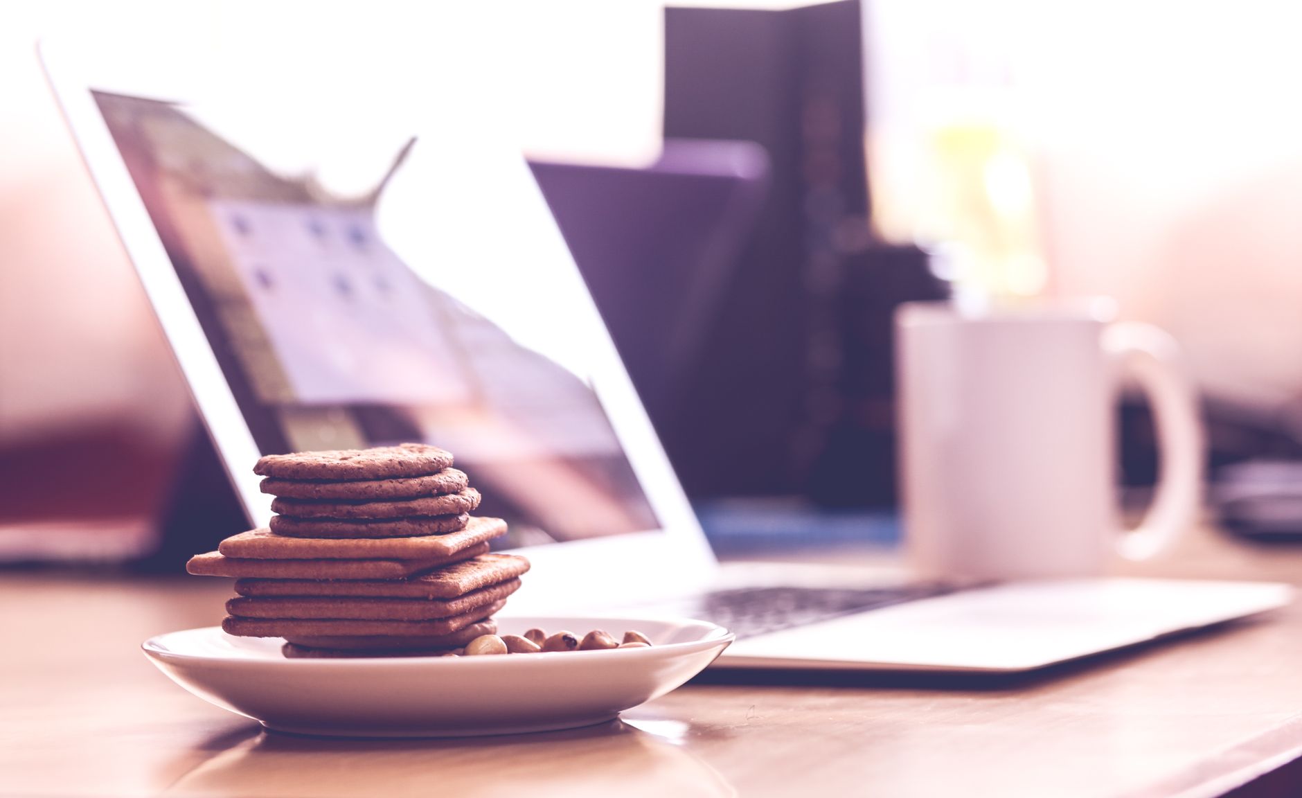 Stack of crispy biscuits on a saucer with a laptop in the background, evoking a cozy workspace vibe.