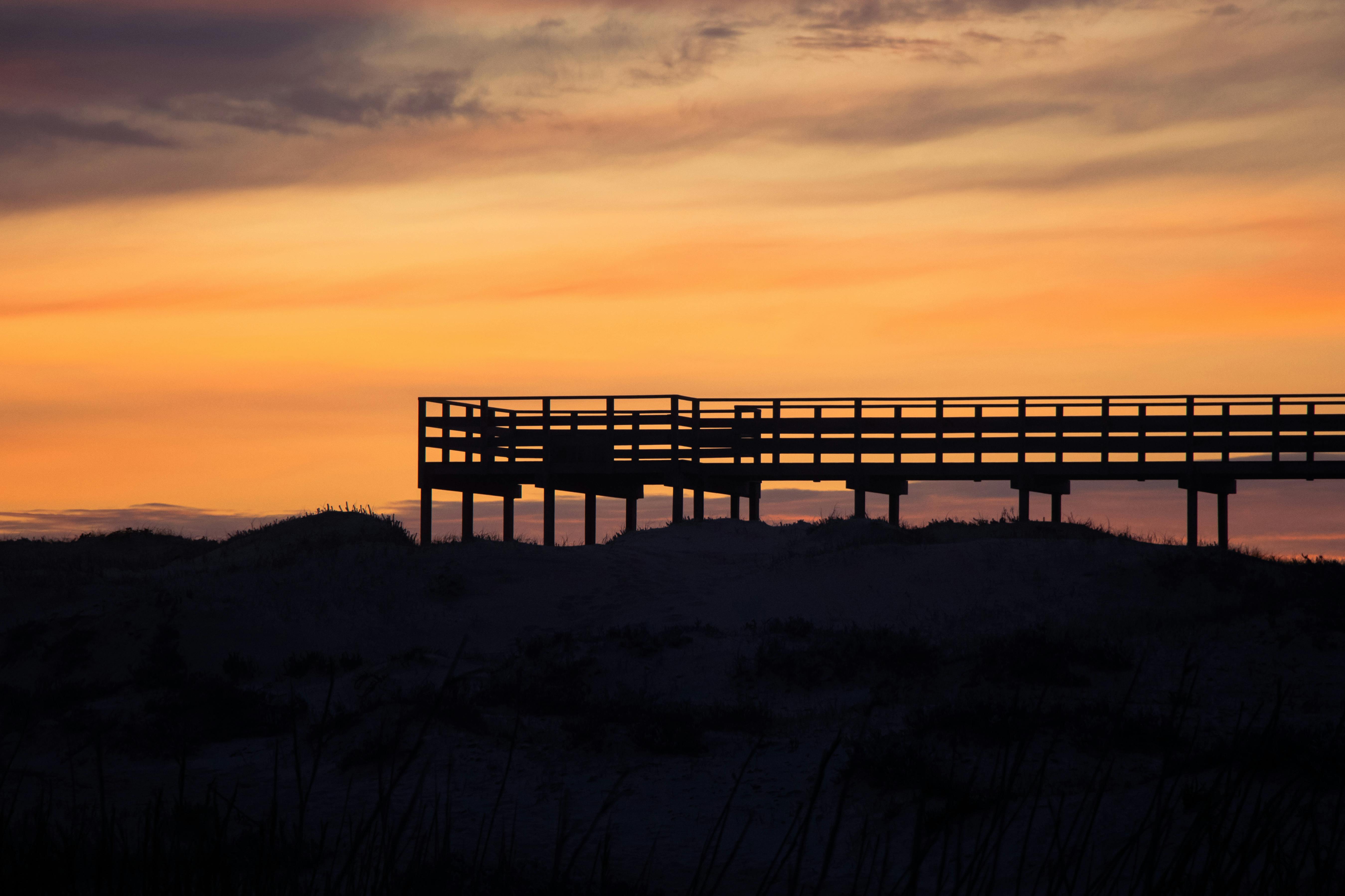 Silhouette of a boardwalk set against a dramatic sunset sky, creating a serene rural landscape.