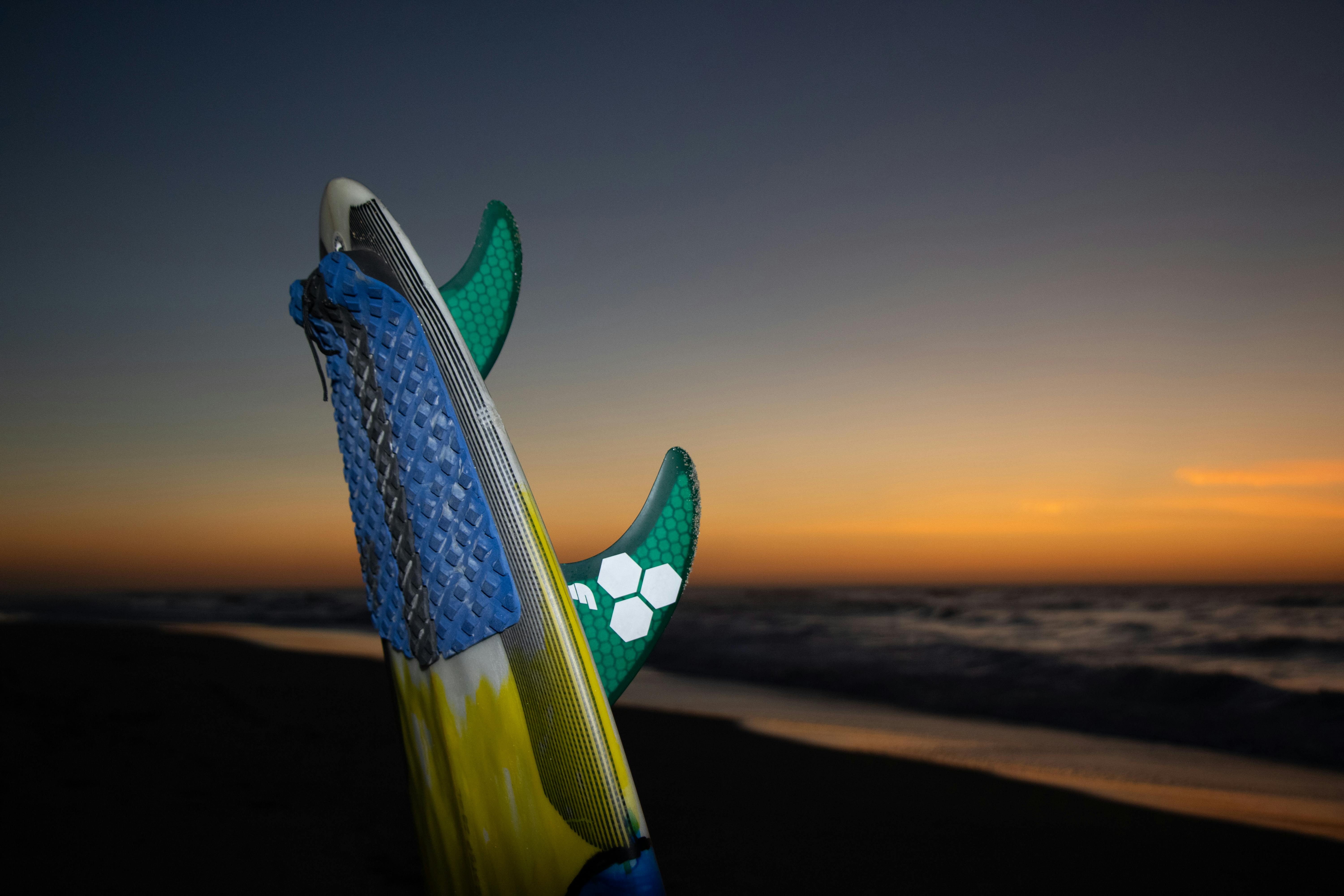Surfboard standing on beach during a vibrant sunset by the ocean surf.
