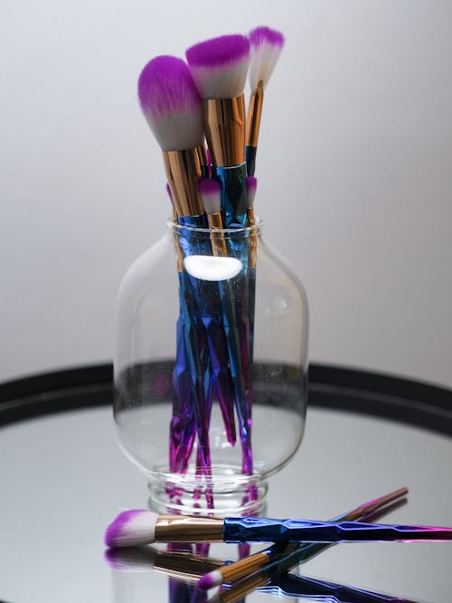 Free A glass vase with purple and blue makeup brushes Stock Photo