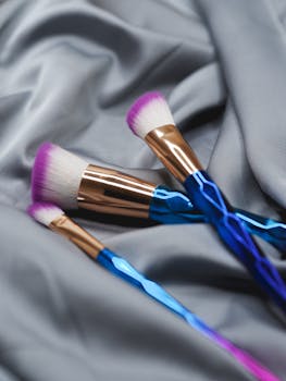 Tri-colored makeup brushes elegantly placed on silky gray fabric, ideal for beauty themes.