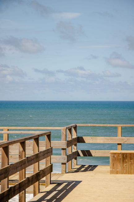 Tranquil wooden pier with railings overlooking the calm blue ocean under a clear sky.