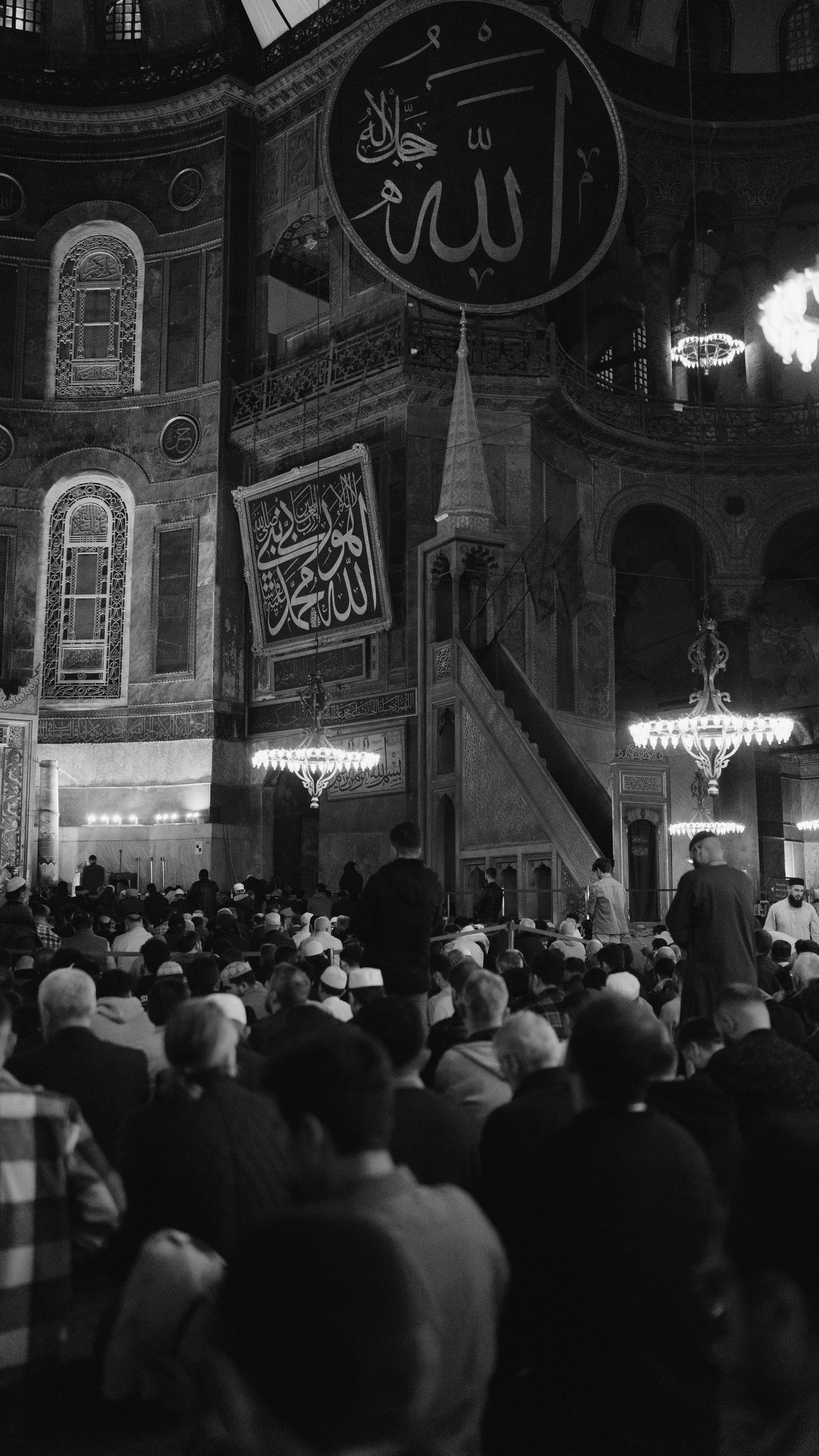 A large crowd in a vast, dim interior, photographed in black and white