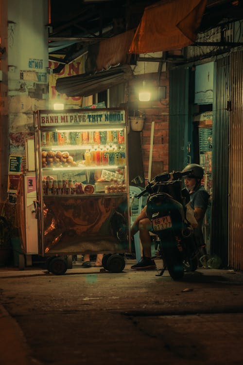 A man sitting on a motorcycle next to a food cart