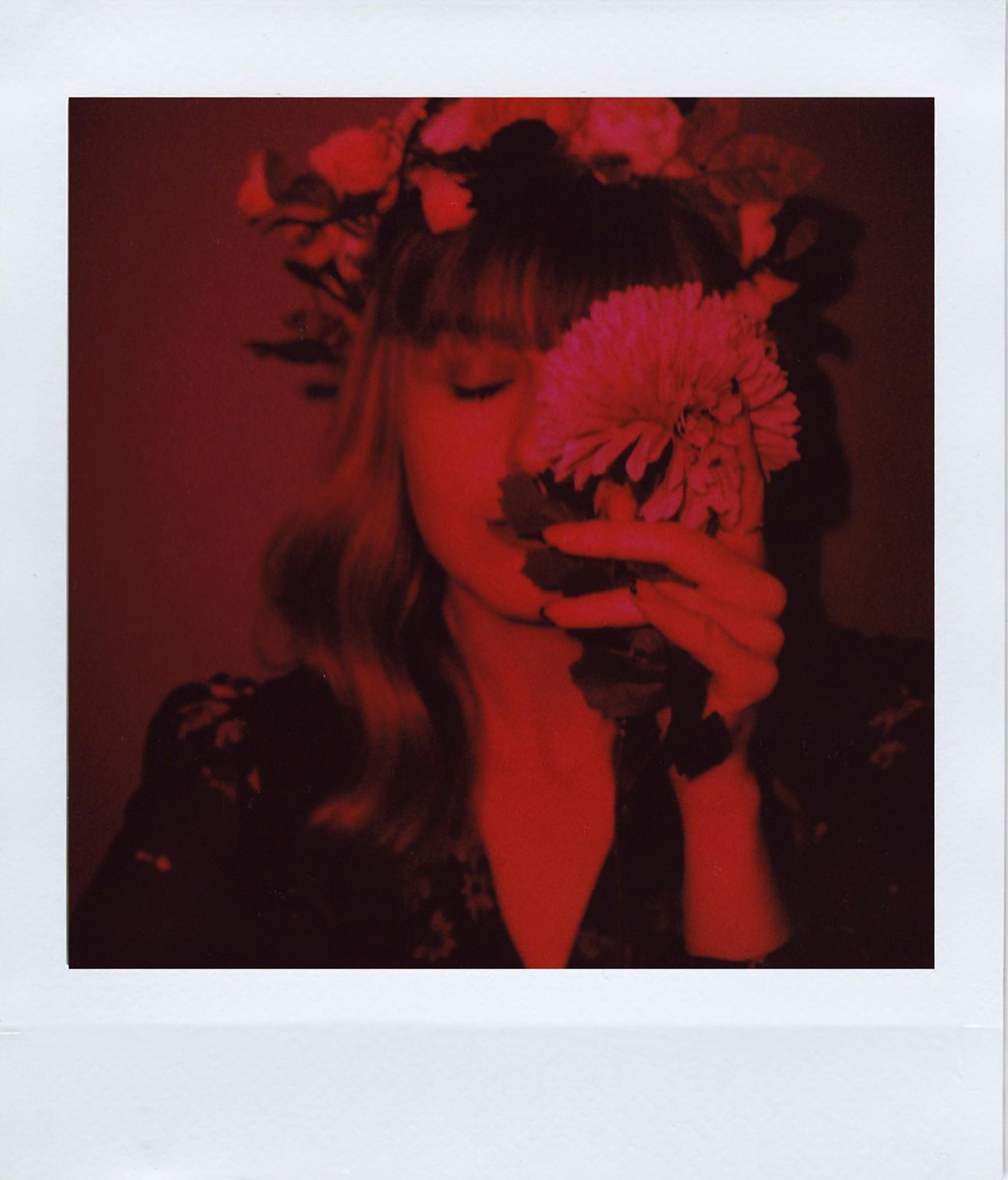 A woman with closed eyes holds a flower, bathed in red light, creating a dreamlike atmosphere.