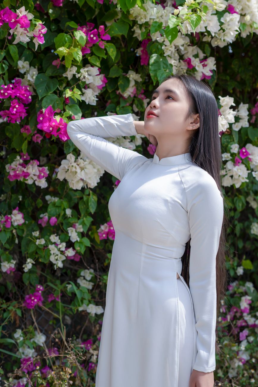 A young woman in a white Ao Dai poses gracefully against a floral backdrop.