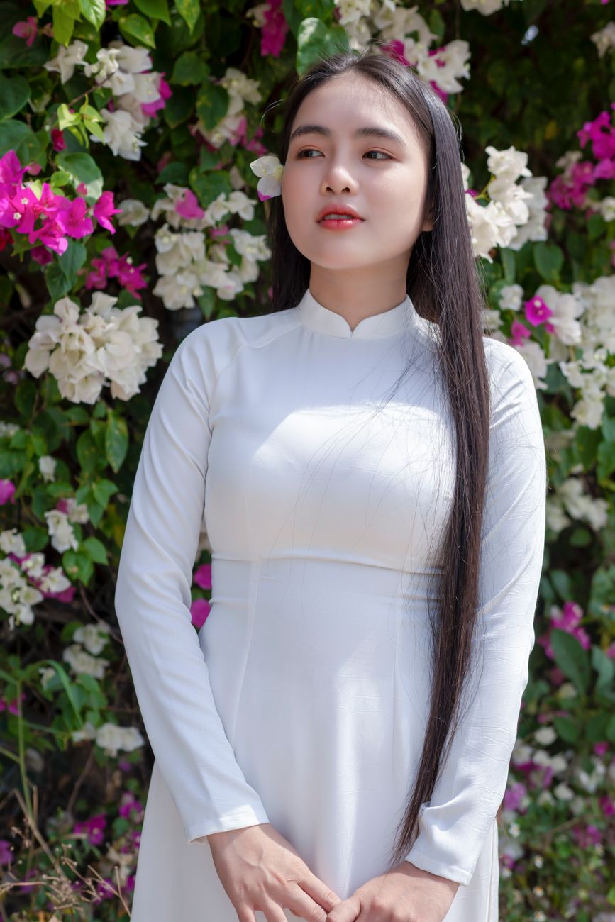 Young woman in traditional Ao Dai dress surrounded by vibrant flowers, showcasing Asian fashion.