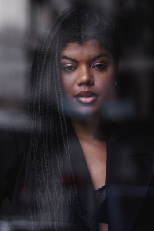 Free Young woman with braided hair stands by a window, deep in thought and reflection. Stock Photo