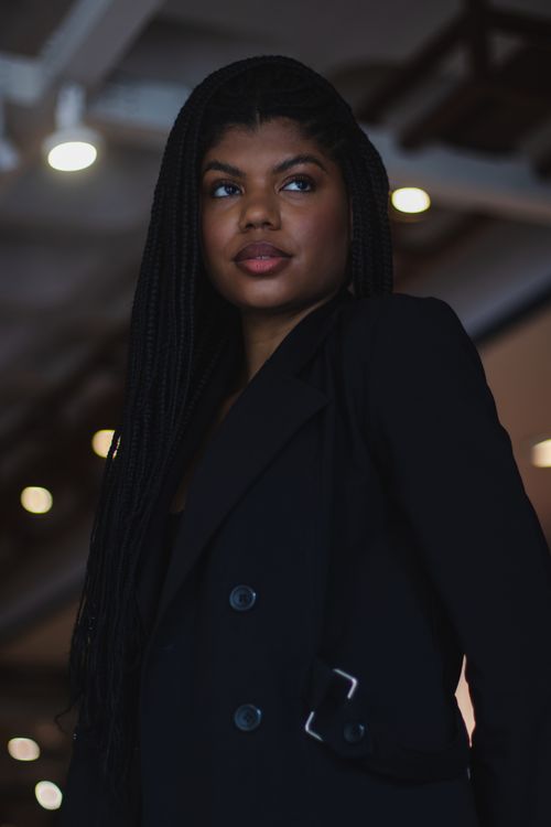 Free Portrait of a stylish woman with braided hair in a chic black jacket, captured indoors in a modern setting. Stock Photo