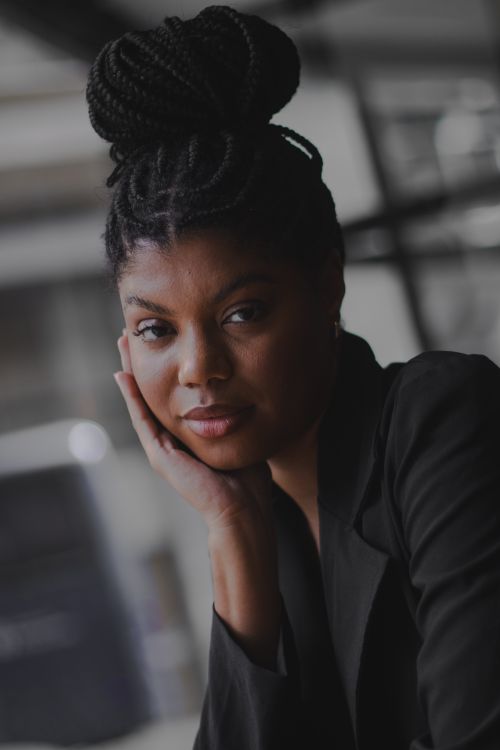 Free Portrait of a serene woman with braided hair in a black blazer, looking thoughtful indoors. Stock Photo