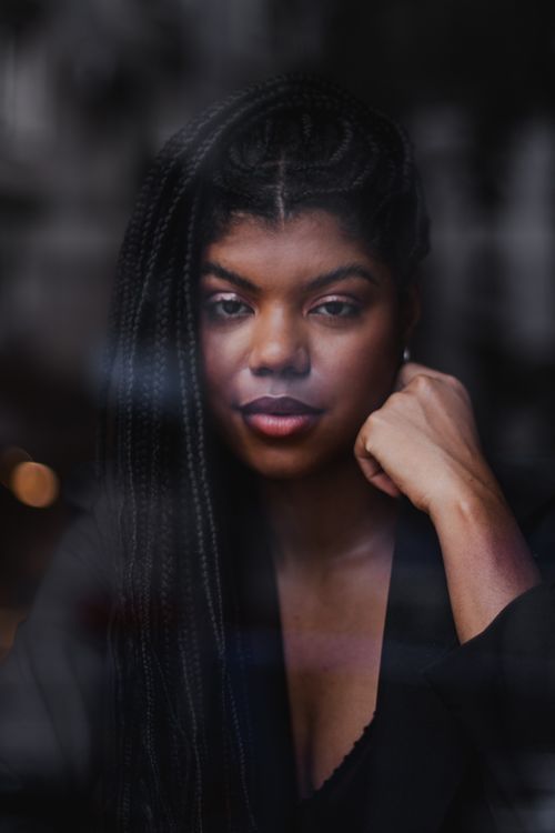 Free Artistic portrait of a thoughtful woman with braided hair looking through a glass window Stock Photo