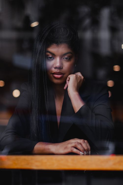 Free Stylish woman with braided hair posing through a café window, creating a reflective mood. Stock Photo