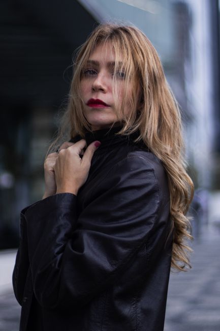 Fotomural Mujer rubia en una chaqueta de cuero negra, posando con confianza en un entorno urbano.