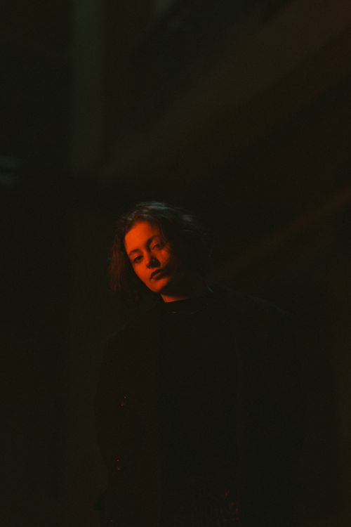 Free A dramatic portrait of a woman under red lighting in a dark studio setting. Stock Photo