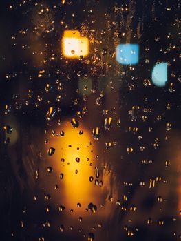 Night scene of raindrops on a window with blurred city lights, creating a moody atmosphere.