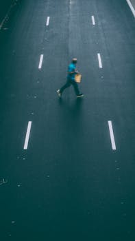 从上方俯瞰，一名背包男子正穿过一条空荡的城市道路，身影略显模糊
