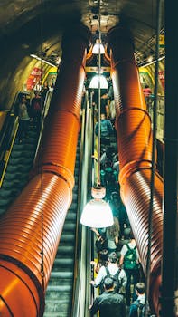 在一个繁忙的城市地铁站，人们乘着自动扶梯，四周环绕着工业管道