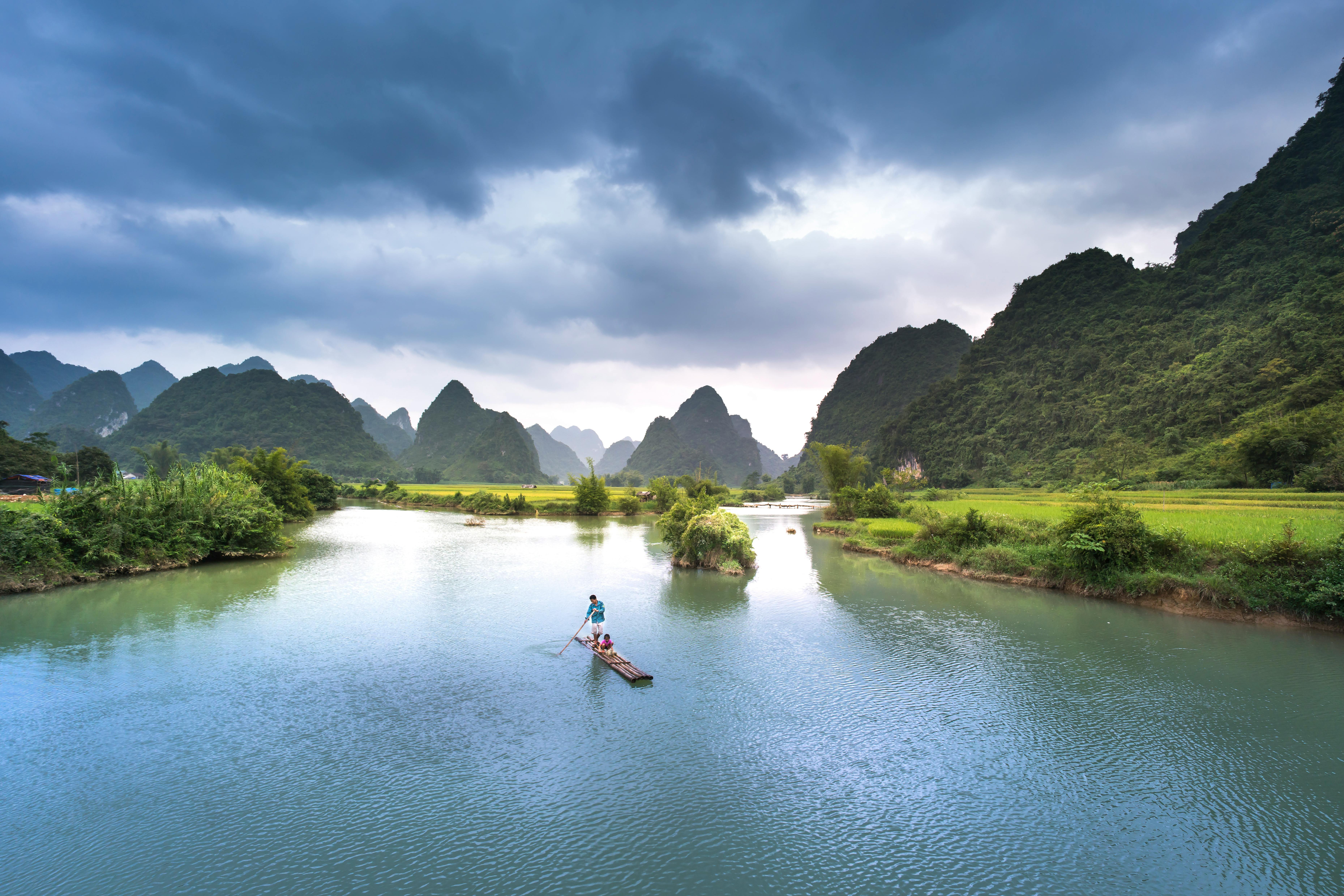 在戏剧性的天空下，一条宁静的河流与郁郁葱葱的绿色山脉相映成趣