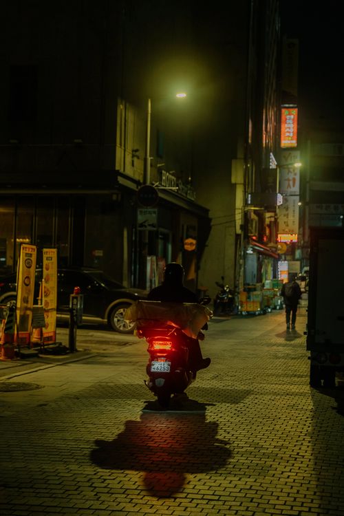 Free A person on a scooter rides through a dimly lit urban street at night. Stock Photo