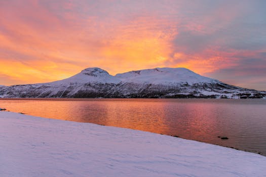 Stunning sunset over snow-covered mountains reflecting in a serene bay in Laksvatn, Norway.