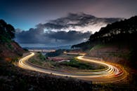 在戏剧性的天空下，蜿蜒的道路上有一条光径，映衬着秀丽的夜景