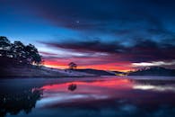 令人惊叹的日落倒映在平静的河流上，天空色彩缤纷，树木的剪影清晰可见