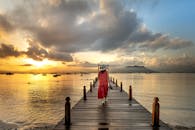 日落时分，海面壮丽，一位身着红裙的女子静静走在码头上