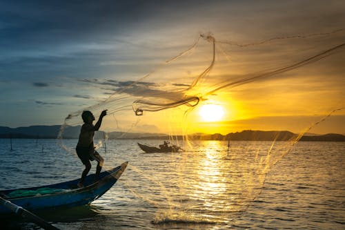Free Man Standing On Boat Throwing Net Stock Photo