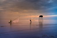 日落时分，两名渔民在海上撒网，映衬着五颜六色的霞光