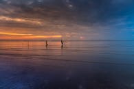 两个渔民在平静的海滩上，迎着充满活力的日落向大海撒网