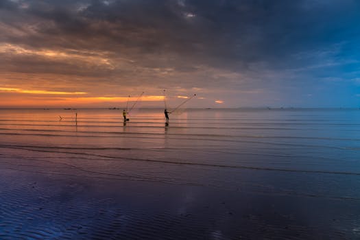 两个渔民在平静的海滩上，迎着充满活力的日落向大海撒网