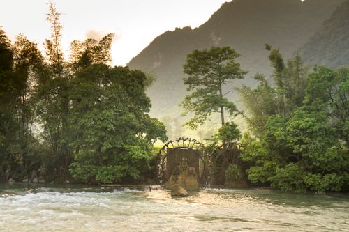 Free Tranquil scene of a river with a water wheel surrounded by lush rainforest vegetation. Stock Photo