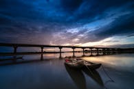 日落时分，一艘船停泊在宁静的河面上，远处是一座雄伟的桥梁