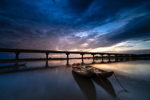 日落时分，一艘船停泊在宁静的河面上，远处是一座雄伟的桥梁