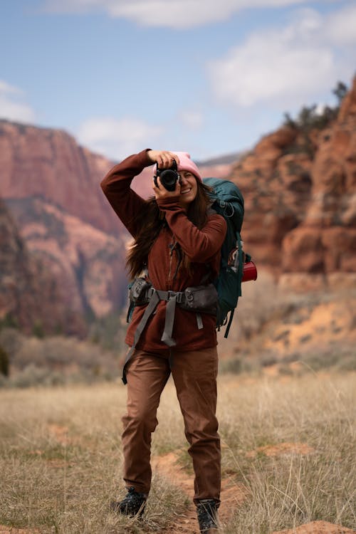 A woman with a backpack taking a picture in the mountains