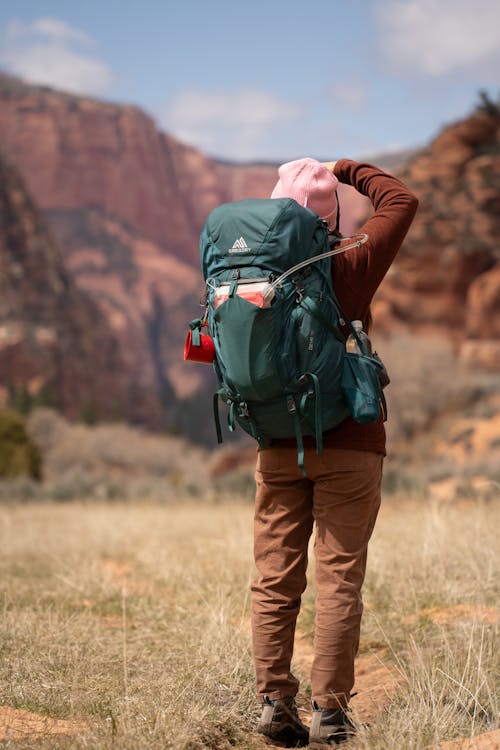 A woman with a backpack on her back is standing in the middle of a field