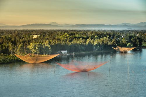 Free Beautiful view of large fishing nets over a tranquil river at sunset, surrounded by lush green trees. Stock Photo