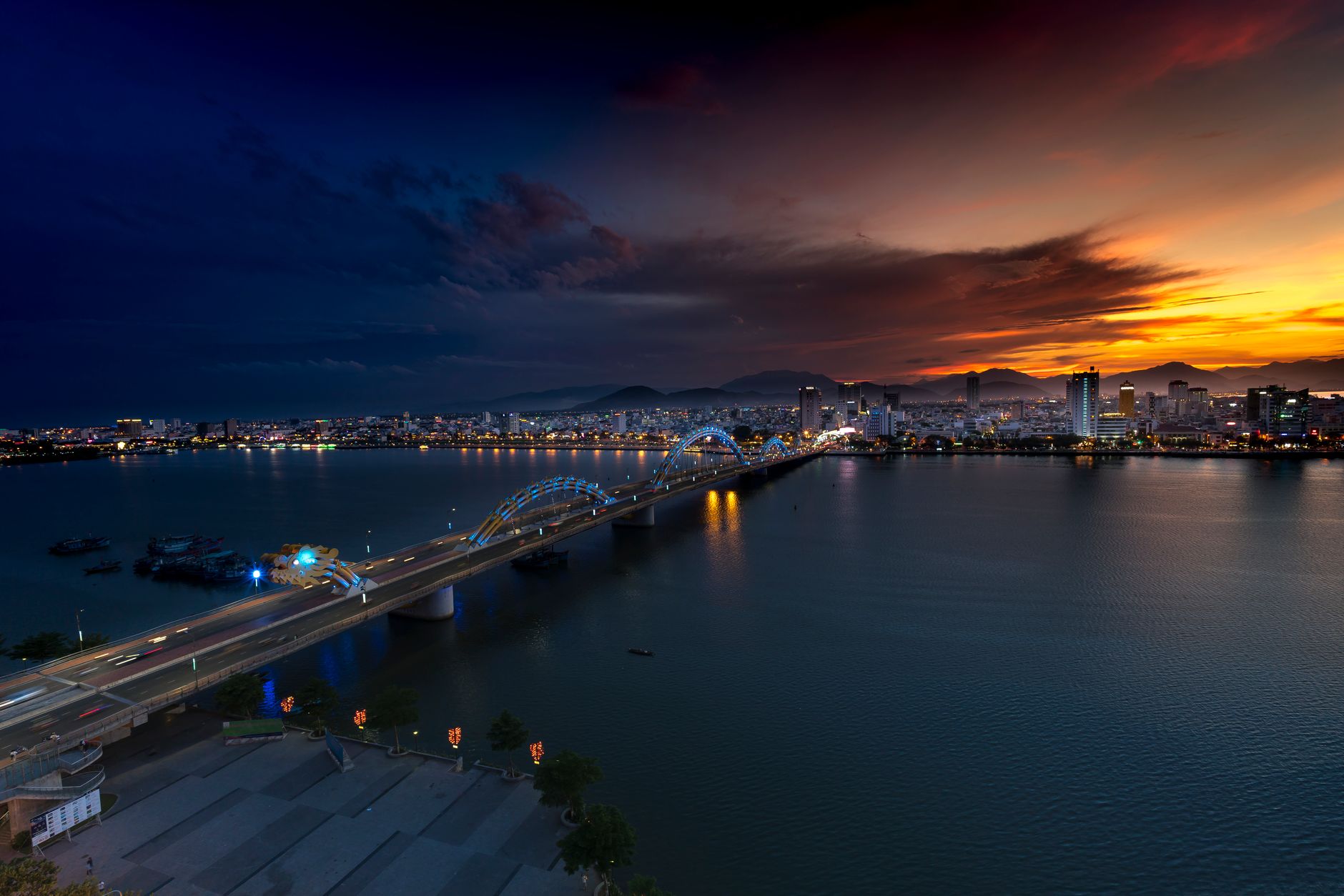 Beautiful panoramic view of a city at sunset with illuminated bridge over the bay, vibrant skyline reflecting on the water.
