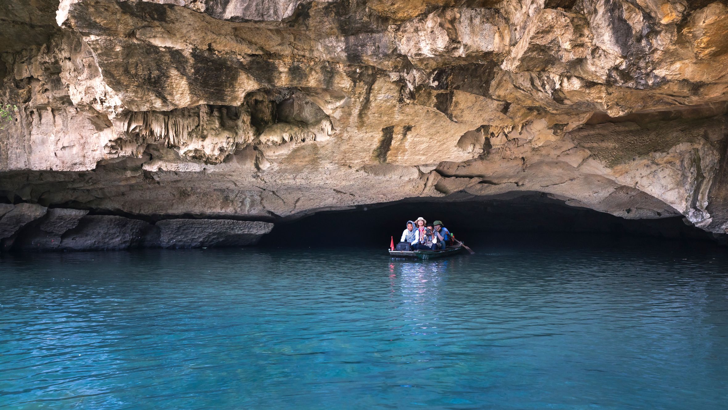 A group of people on a boat exploring a scenic limestone cave with clear blue waters.