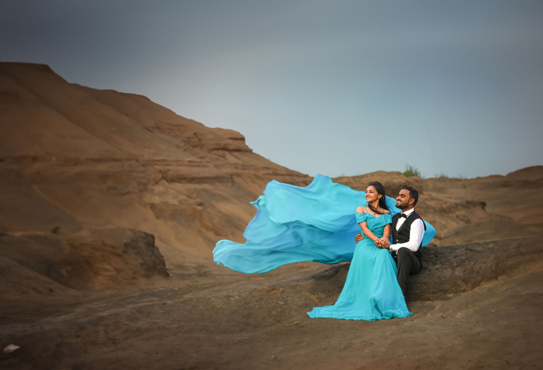 A couple in elegant clothing sitting on sand dunes, capturing a serene desert scene near Pune, India.