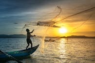 日出时分，一名渔夫熟练地将网撒向湖面，金色的天空映衬着平静的湖水