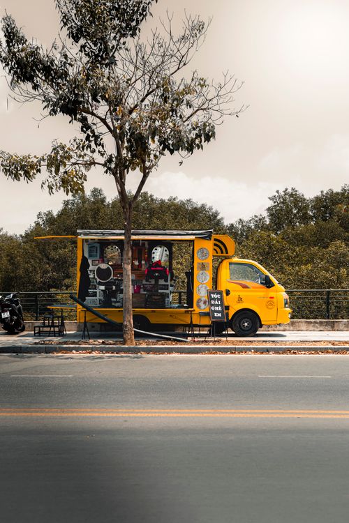 Free Yellow coffee truck parked on a vibrant urban street in Ho Chi Minh City, offering refreshments. Stock Photo