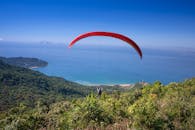 滑翔伞翱翔在郁郁葱葱的绿植与蔚蓝大海构成的沿海景观之上