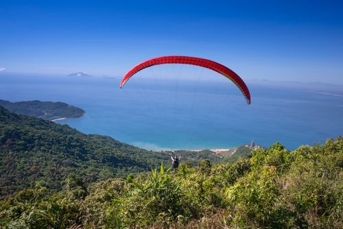Free A paraglider soaring above a coastal landscape with lush greenery and blue sea. Stock Photo
