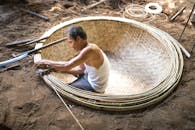 一位亚洲老人在户外阳光下编织一个大竹篮