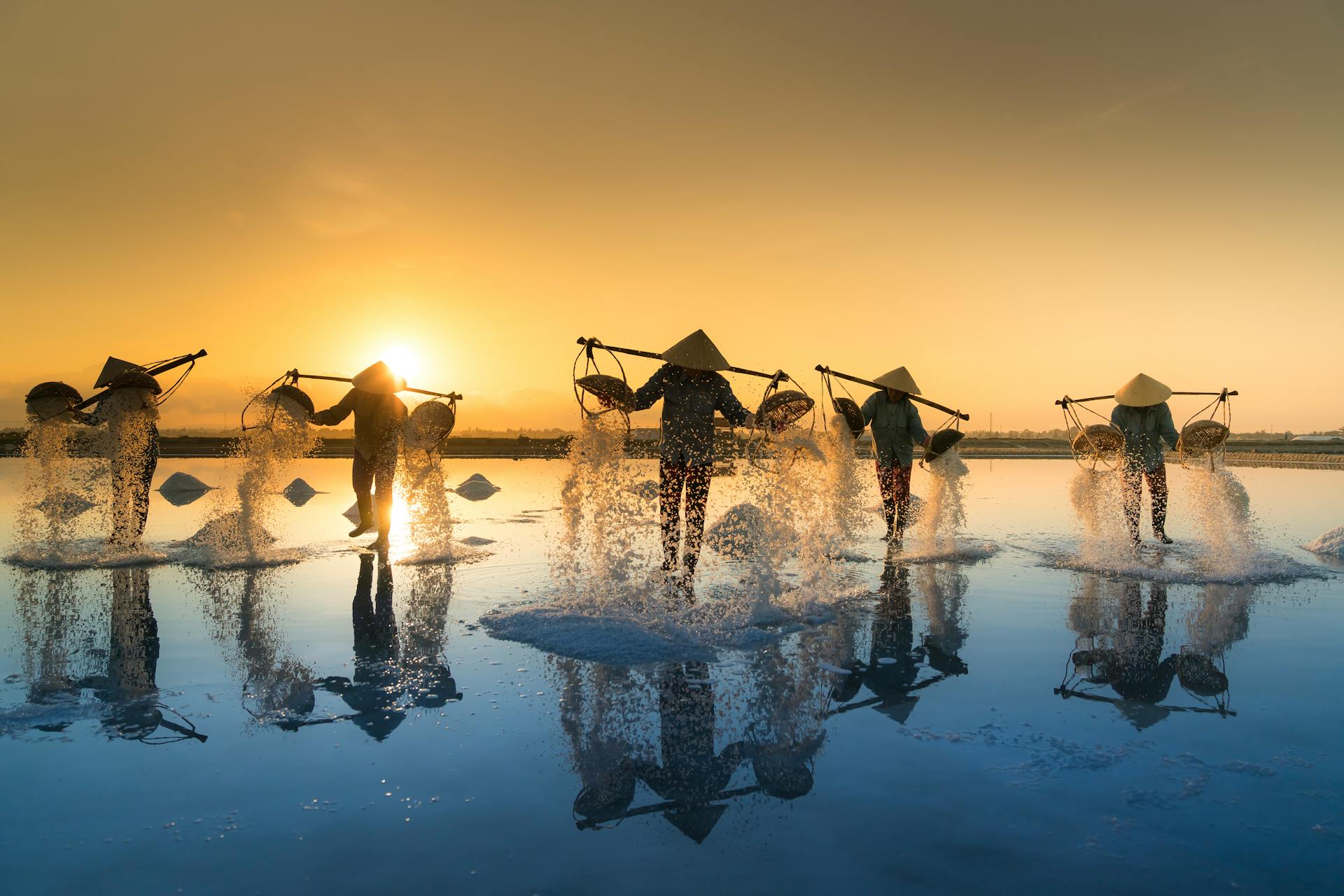 People Pouring Sea Water on Salt Field during Sunset